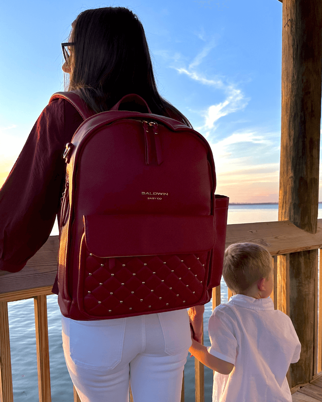 Baldwin Baby Company Daphne diaper bag in crimson shown in a sunset lifestyle setting