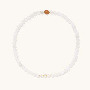 Three layered white beaded bracelets with carved orange agate lotus centerpiece and freshwater pearls on cream background.