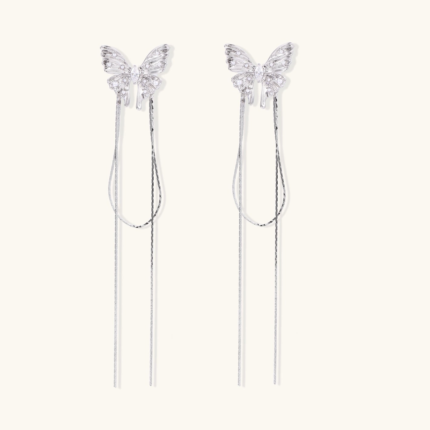 Pair of silver threader earrings with crystal butterfly tops and long chain drops on cream background.