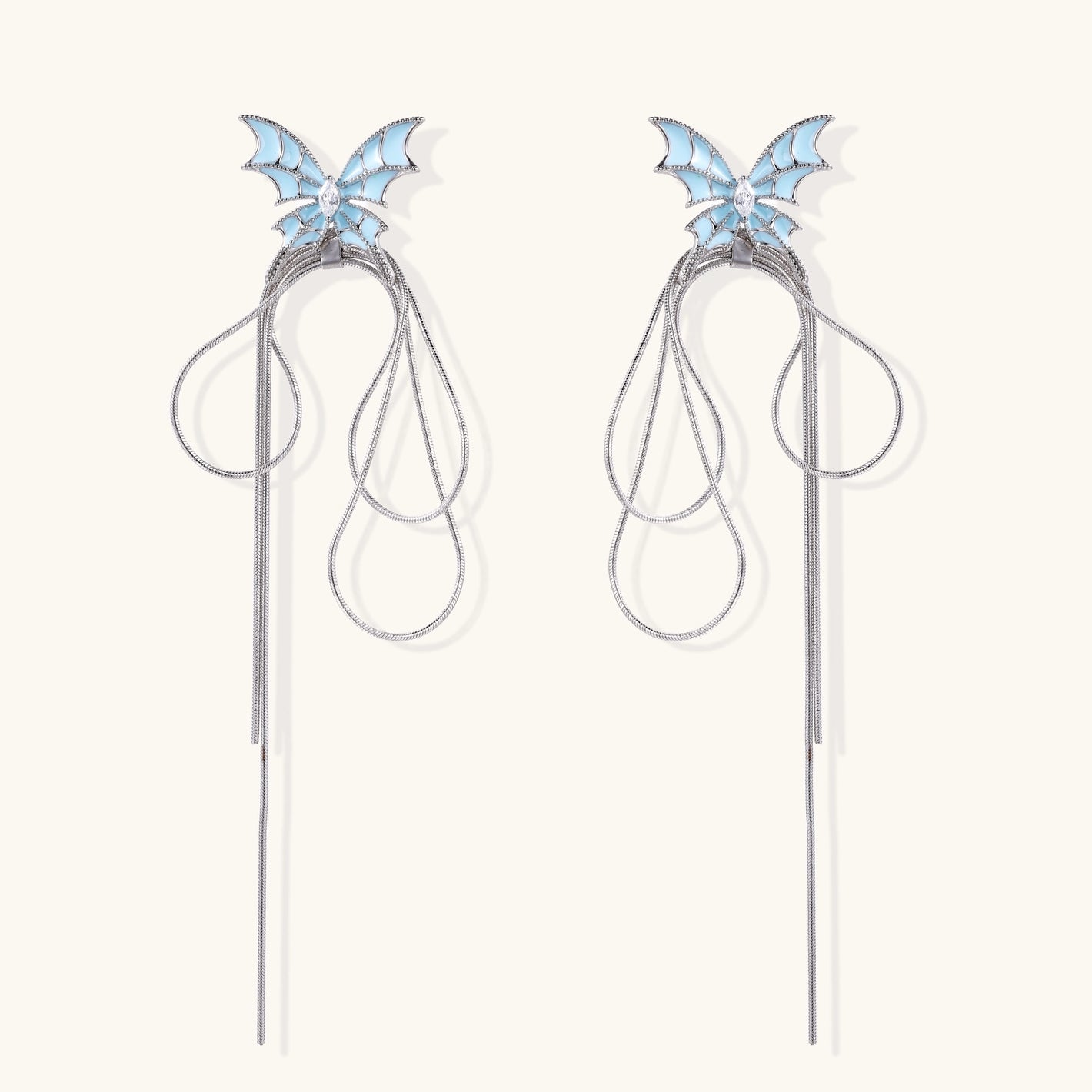 Long silver-tone earrings with powder blue enamel butterfly studs and flowing chain tassels on cream background