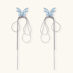 Long silver-tone earrings with powder blue enamel butterfly studs and flowing chain tassels on cream background