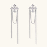 White gold plated baroque cross stud earrings with long cascading zirconia chains on cream background