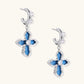 Silver hoops with denim-inlaid cross charms and clear crystals on beige background