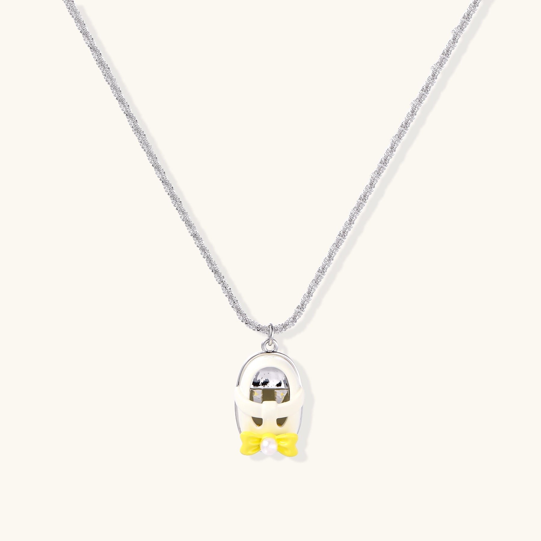 Chrome egg-shaped pendant with kawaii face, yellow bow, and pearl detail on silver chain against white background