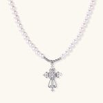 White pearl necklace with ornate silver cross pendant featuring zirconia crystals on cream background.