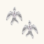 White gold-plated bird earrings with spread wings and oval zirconia center on cream background