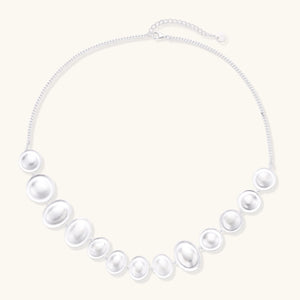 Graduated pearl-finish silver discs forming an organic bubble bib necklace on delicate chain against cream background.
