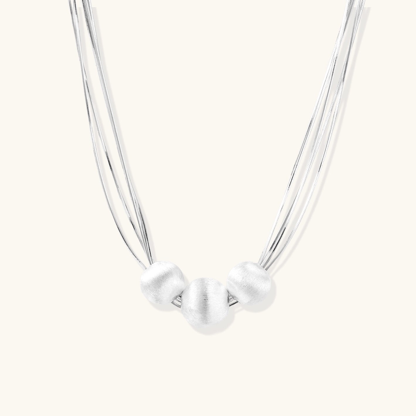 Sterling silver multi-strand necklace with three brushed round beads on cream background