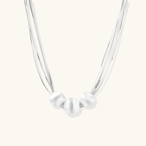 Sterling silver multi-strand necklace with three brushed round beads on cream background