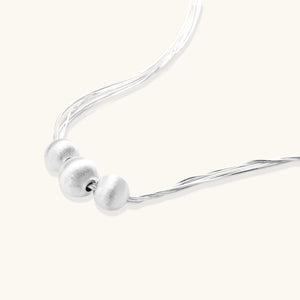 Sterling silver multi-strand necklace with three brushed round beads on cream background