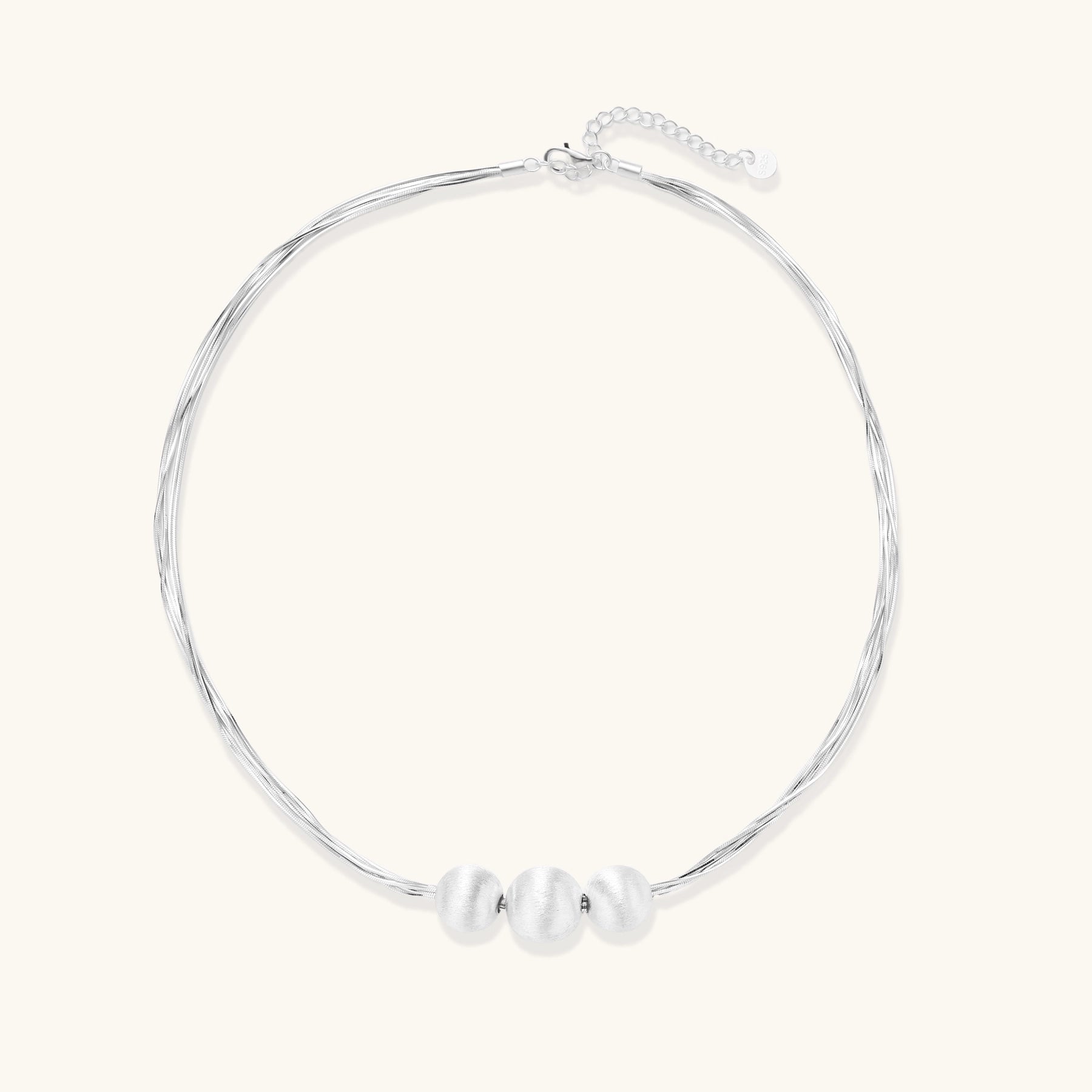 Sterling silver multi-strand necklace with three brushed round beads on cream background