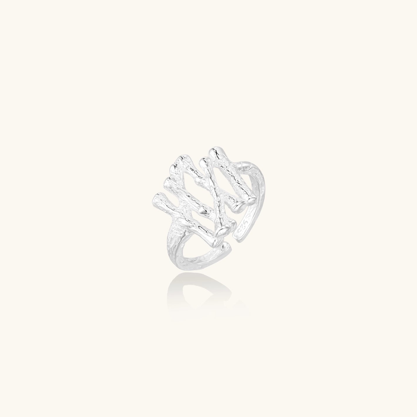 Sculptural sterling silver ring with organic branch design and textured surfaces on cream background
