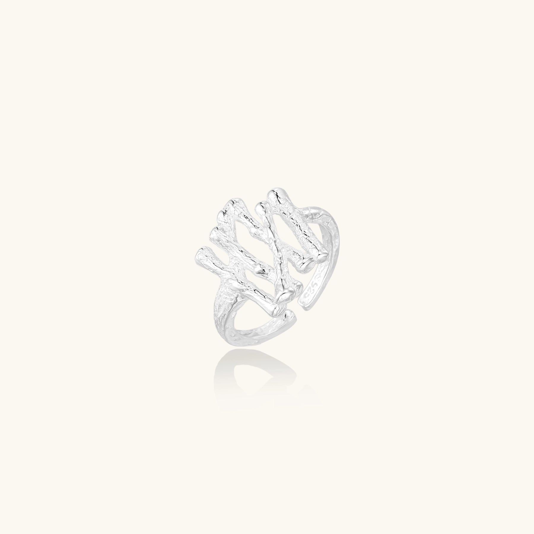 Sculptural sterling silver ring with organic branch design and textured surfaces on cream background