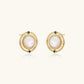 Circular gold stud earrings with iridescent mother-of-pearl center and green zirconia accents on cream background.