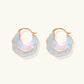 Shell-shaped hoop earrings with iridescent blue-pink enamel and gold trim on cream background