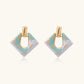 Geometric square enamel earrings with marbled turquoise and lavender pattern, gold U-shaped connector on cream background.