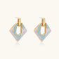 Geometric square enamel earrings with marbled turquoise and lavender pattern, gold U-shaped connector on cream background.