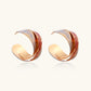 Sculptural gold-plated hoop earrings with diagonal purple and coral enamel stripes in twisted ribbon design