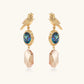 Gold-plated bird stud earrings with iridescent abalone shell medallions and champagne crystal drops on cream background