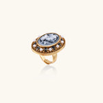 Gold-plated ring with oval blue floral cameo, pearl accents, and black enamel detailing on white background.