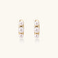14K gold-plated curved stud earrings with three white freshwater pearls aligned vertically on cream background