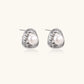 Triangular white gold plated stud earrings with central freshwater pearl and baguette-cut stones on white background