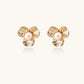 Gold-plated flower stud earrings with textured petals and centered freshwater pearl on beige background