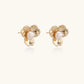 Gold-plated flower stud earrings with textured petals and centered freshwater pearl on beige background