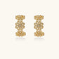 Gold hoop earrings with intricate three-dimensional floral filigree pattern in 14K gold plated brass on cream background
