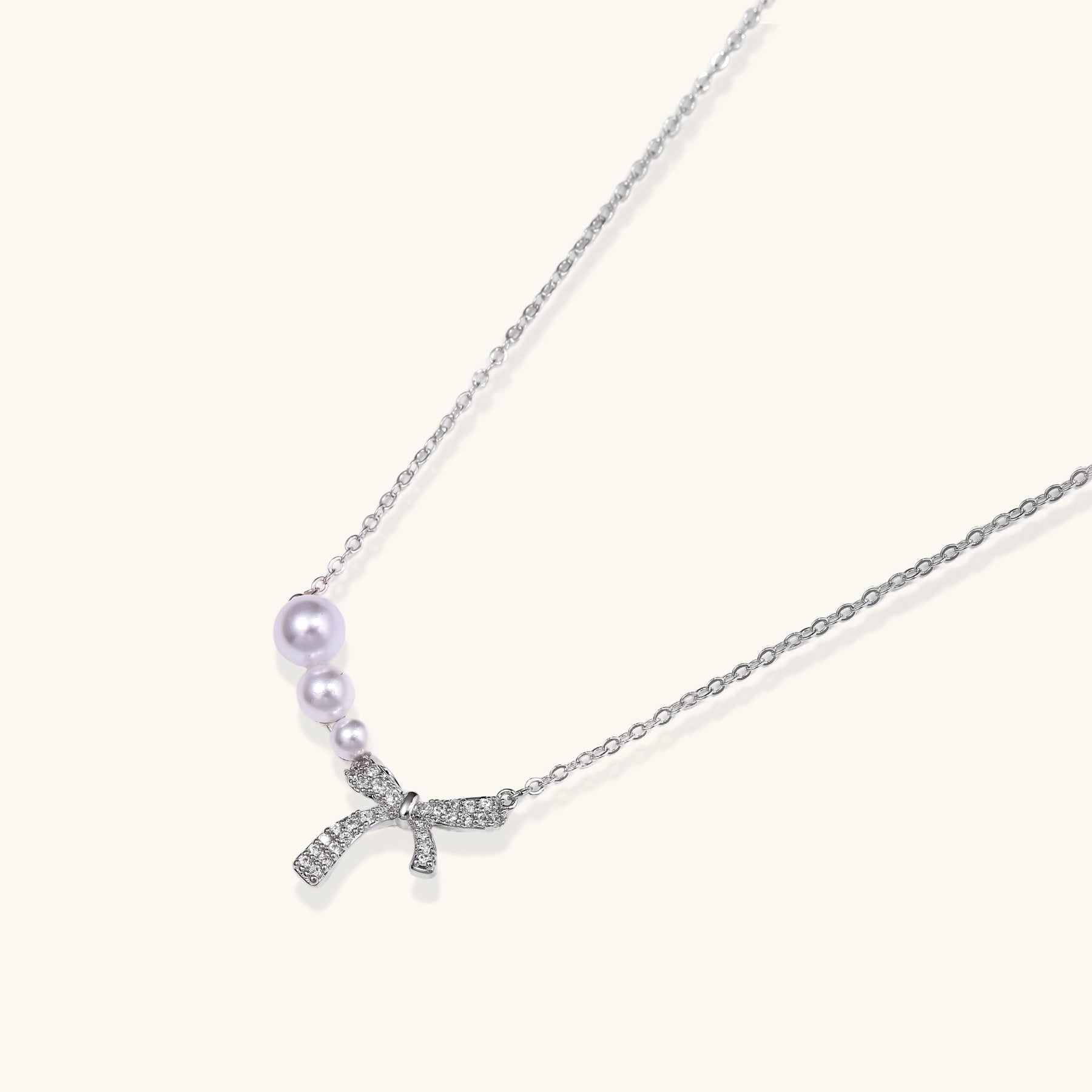 Delicate white gold plated necklace with freshwater pearls and sparkly crystal bow pendant on white background