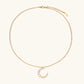 Gold crescent moon pendant with graduated white pearls on delicate chain against cream background