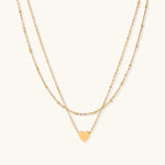 Delicate double-chain gold necklace with tiny heart pendant on cream background