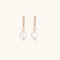 Gold huggie hoop earrings with pavé crystals and white freshwater pearl drops on cream background