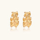 Pair of gold huggie hoops with sculpted wave texture and dimensional ripples on neutral background.