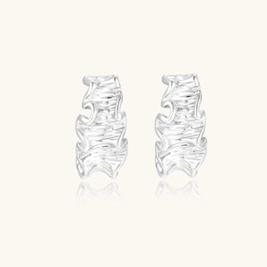 White gold plated sculptural hoop earrings with organic wavy edges and reflective metallic finish on cream background