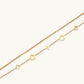 Double-layer gold-plated bracelet with quatrefoil and star charms on cream background, 18K gold finish.