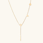 Gold Y-shaped necklace with L-O-V-E letter charms and vertical bar pendant on delicate chain against cream background