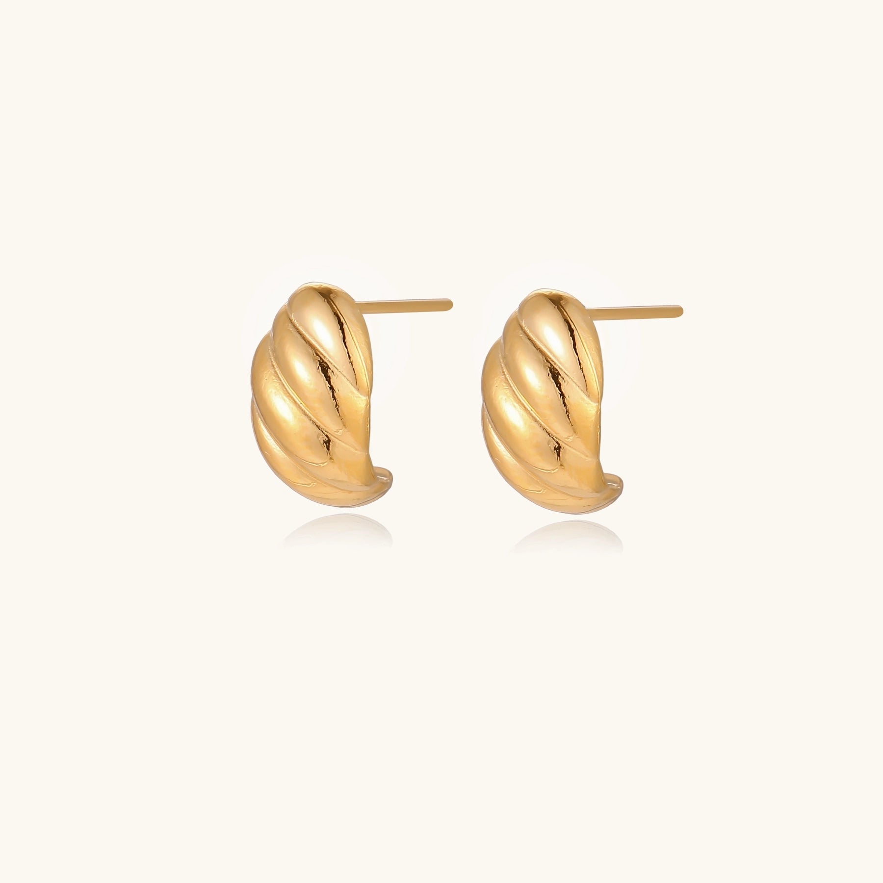 Chunky gold twisted rope huggie hoops with diagonal grooves and high-polish finish on cream background