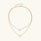 Gold layered necklace set with sunburst and smiley face pendants on delicate chains against white background.