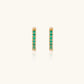 Pair of small gold huggie hoop earrings with bright green cubic zirconia stones on cream background