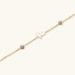 Gold chain bracelet with white mother of pearl butterfly pendant and two bezel-set crystals on cream background