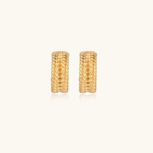 Textured gold huggie hoop earrings with raised ribbed rows creating dimensional sculptural design on cream background