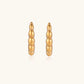 Gold-plated chunky hoop earrings with ridged bubble texture on cream background