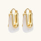 Sculptural gold-plated hoop earrings with flowing curved design and lever-back closure on cream background.