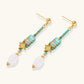 Gold-plated dangle earrings with turquoise threading, star charms, and white pearl beads against cream background.