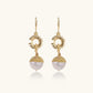 Gold sunburst charm earrings with baroque pearl drops on French hooks against cream background
