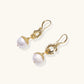 Gold sunburst charm earrings with baroque pearl drops on French hooks against cream background