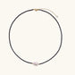 Delicate necklace with black blue sandstone beads and baroque pearl center on white background with gold accents.