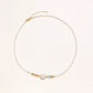 Delicate white beaded necklace with baroque pearl center, gold accents, and coral and aqua gemstones on cream background.