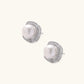 Rhodium-plated sterling silver stud earrings with round freshwater pearls surrounded by geometric crystal halos on cream background.